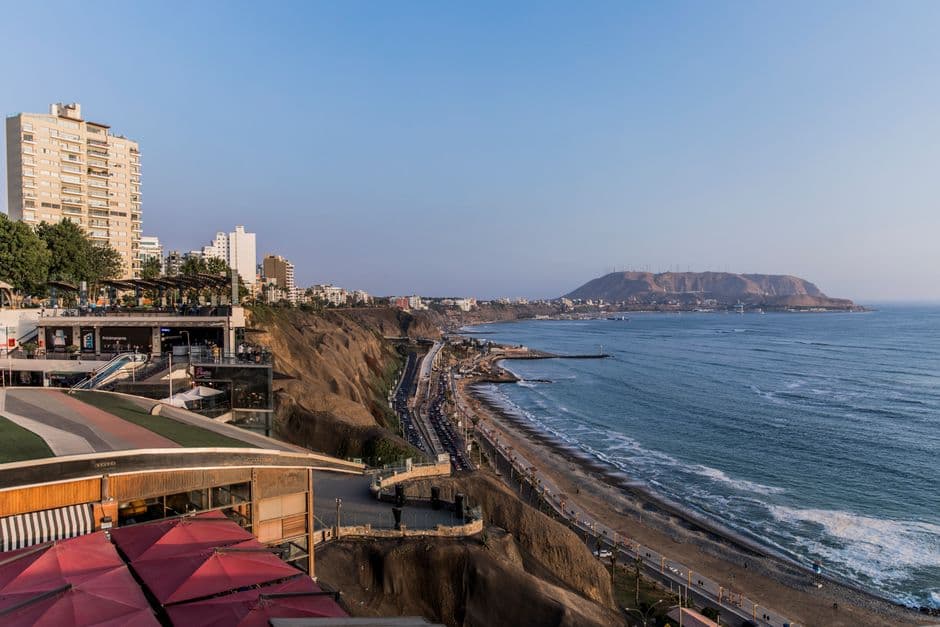 The cliffs of Miraflores in Lima above the Pacific Ocean, with a clifftop terrace, the coastal highway and beach below, and a headland across the bay