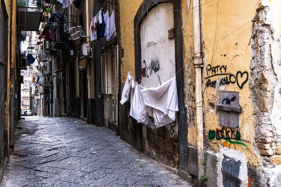 A narrow street in the historic center of Naples with laundry strung between the buildings above and graffiti on the walls
