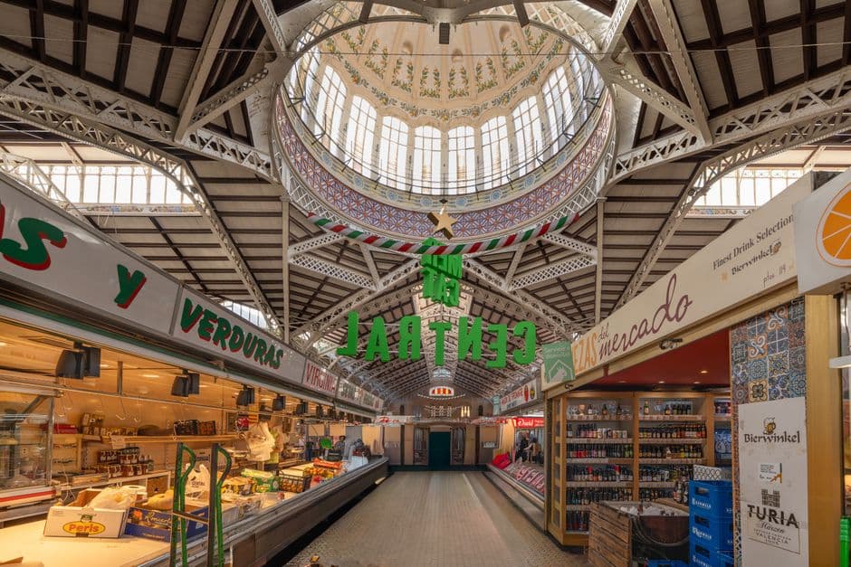 Inside the Mercat Central in Valencia, with an iron and glass roof, a painted dome and green hanging letters spelling Mercat Central above the aisle of stalls