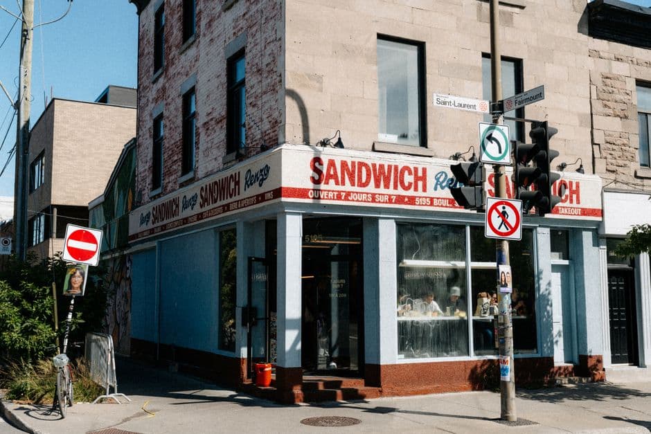 Corner sandwich shop with a red and white awning reading SANDWICH, at the intersection of Boulevard Saint-Laurent and Fairmount Avenue in Montreal