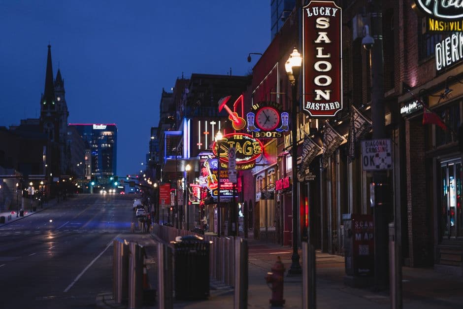Lower Broadway in Nashville at blue hour, neon bar signs lit along the street with the downtown skyline behind