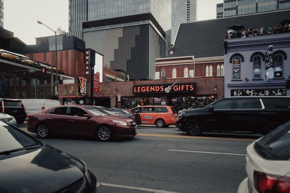 Traffic on Lower Broadway in Nashville in daylight, with the Legends Corner gift store sign and the National Museum of African American Music behind