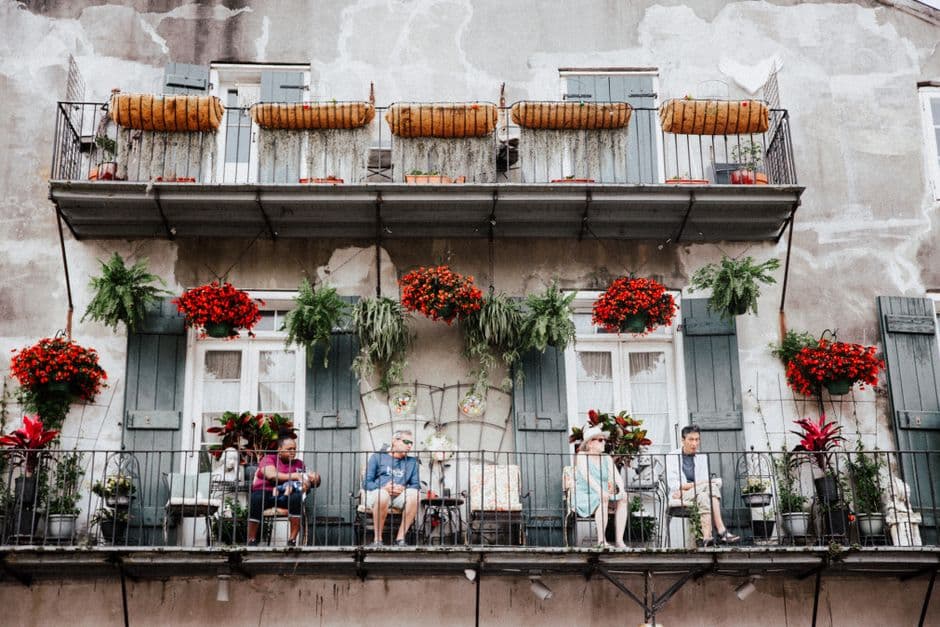 Four people sitting out on a French Quarter balcony in New Orleans, with green shutters, wrought iron railings and hanging ferns