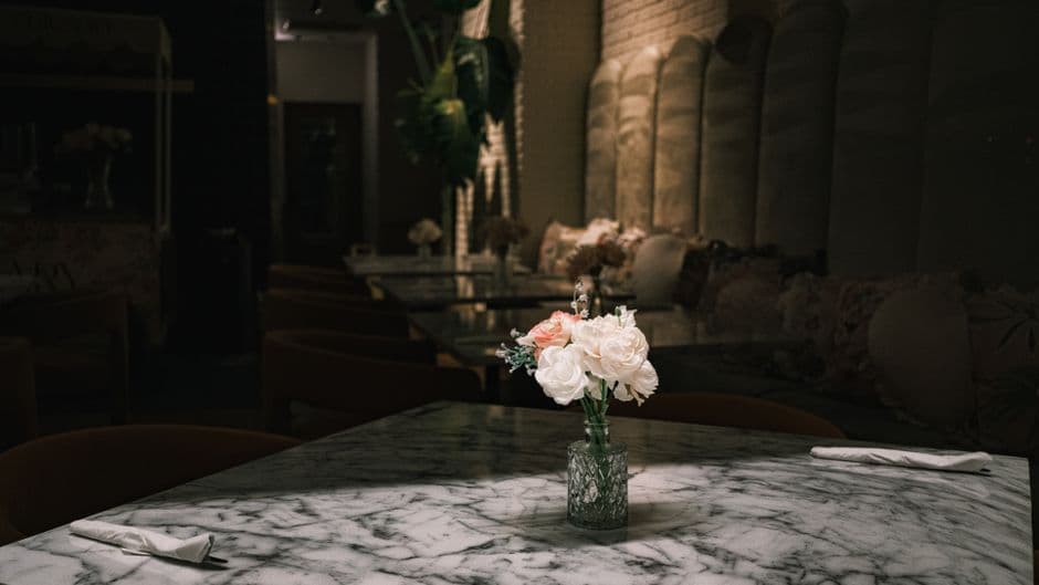 A marble café table with a small vase of flowers and folded napkins in a dimly lit dining room
