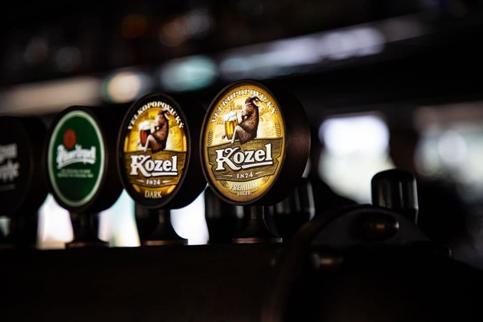 A row of beer taps in a dark Czech pub with Velkopopovický Kozel and Pilsner Urquell badges in focus